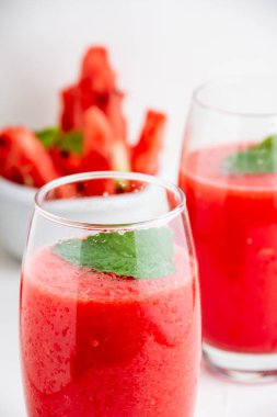 İki bardak karpuz suyu, nane şekeri ve karpuz parçalı kase, masa ve beyaz arka planda seçici odak, dikey olarak.