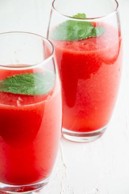 Nane yaprağıyla iki bardak karpuz suyunun üst görüntüsü, seçici odak, masa ve beyaz arka plan, dikey