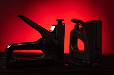 Zımbalı ahşap bir masada iki gümüş inşaat zımbası, kırmızı arka planda, yakın planda.