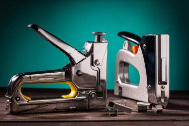 Zımbalı ahşap bir masada yeşil arka planda, yakın planda iki gümüş inşaat zımbası.