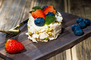 Tahta bir tepside altın çatallı kremalı pasta rulosu. Çilek, yabanmersini ve nane. yakın plan.