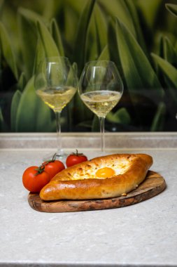 Tahta tepside yumurtalı Khachapuri, şarap ve domatesli, yakın plan..