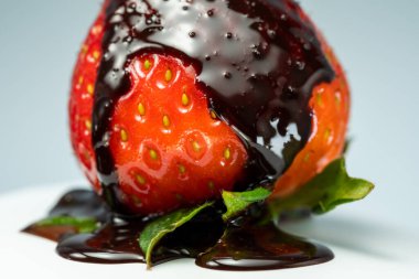 Yeşil yapraklı taze çilekler, üzerine çikolata dökülmüş, beyaz arka planda, yakın plan..