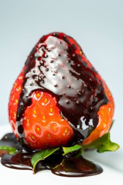 Yeşil yapraklı taze çilekler, üzerine çikolata dökülmüş, beyaz arka planda, yakın plan..