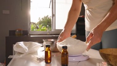 Beyaz kaseden gümüş çömleğe soya yağı döken kadın yavaş çekim arkasında güneş ışığı olan ev yapımı mum sanatları konsepti.