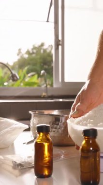 Dikey video. Beyaz kaseden gümüş çömleğe soya yağı döken kadın yavaş çekim arkasında güneş ışığı olan ev yapımı mum sanatları konsepti.