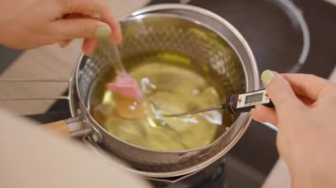 Erimiş soya ağdasının spatulayla karıştırılmasının en üst görüntüsü sıcaklığın dijital termometreyle ölçüldüğü kabın içinde. DIY Craft kavramını kabul et