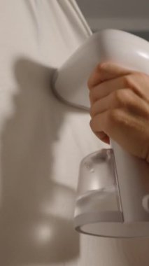 Dikey video. Beyaz Giysi Buharlı Buharlı Bir Elin Yakın Çekimi Küçük Aydınlatma Odasında, Yan Açı, Yavaş Hareket, Ev İşleri Konsepti