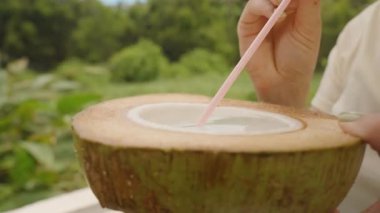 Hindistancevizini iki eliyle tutarken Çubuktan Hindistan Cevizi Suyu İçen Kadın 'ın Yakın Çekimi Açık Hava Ayarları, Yan Açı, Gerçek Zaman, Doğal Su Konsepti