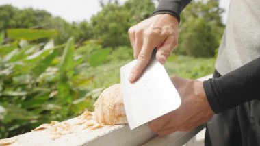Arka planda yeşil ağaçlar olan Balkon Duvarında, Cleaver 'ı kullanarak hindistan cevizi kabuğunu traş etmek, yavaş çekim açı, Yemek Sanatı Kavramı