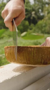 Dikey video. Bir hindistan cevizini yarı yarıya bölen kişi Çimento Ledge in a Lush in a Lush Outdoor Setting, Orta Açı, Sağlıklı Yeme Konsepti