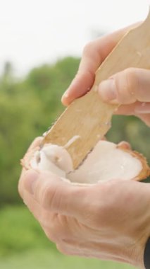 Dikey video. Yarım Deniz Kabuğundan Hindistancevizi Kazıyan Kişi Yeşil Arka plan, Kapalı, Sağlıklı Yeme Konsepti ile Açık Hava Parmaklarını Kullanıyor