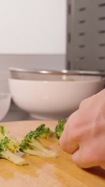 Dikey video. Bright Kitchen 'daki Ahşap Kesme Tahtasında Arka planda Lavabo ile Yavaş Çekim Brokoli Kesimi