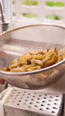 Dikey video. Metal Süzgecin İçindeki Midyeleri Elle Fırlatmak Lavabonun Üzerinde Su Damlacıkları Düşerken, Mutfak Arkaplanı