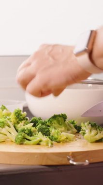 Dikey video. Ön planda Bıçakla Kolander 'a Doğramalı Brokoli Yerleştiren Kadın Arka Görünümü, Arkaplanda Lavabo, Sağlıklı Yemek Kavramı