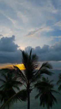 Dikey video. Avuç içlerinden süzülen Hava Aracı Tropikal Okyanus 'un üzerinde yakıcı günbatımına doğru Geniş Bulutlu ve Yansıtıcı Suyla