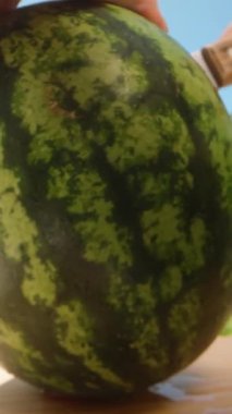 Dikey video. Mavi Gökyüzü ve Yeşil Ağaçlar ile Parlak Dış Sahne 'de Tahta Yüzeyde Taze Karpuz Kesen Ellerin Kapanışı, Taze Meyve Kavramı