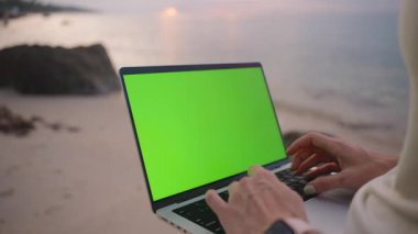 Eller laptopta, okyanusa bakan yeşil ekranlı daktilo, yakın açı, çevrimiçi iş kavramı