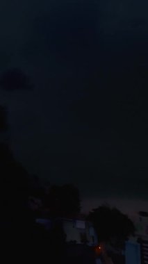 Dikey video. FPV Drone Karanlık Kıyı ve Okyanusa Dalarken Kıyı Köyünün Işıklarını Yakalıyor, Dramatik Hava Batımı Sahnesi