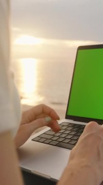 Dikey video. Sunset Beach 'te dizüstü bilgisayarla yazılan eller alçak açılı, uzaktan çalışma konsepti