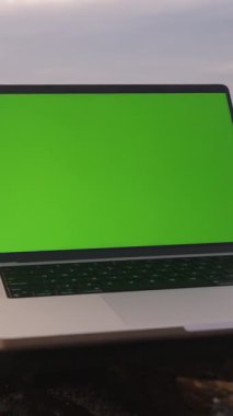 Dikey video. Yeşil Ekranlı Laptop Sahilde Kaya 'da, Arkaplanda Okyanus, Geniş Açı, Teknoloji Konsepti