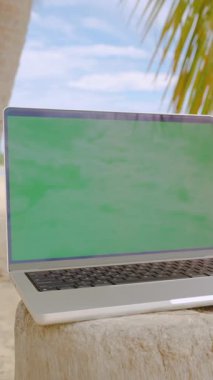 Dikey video. Boş Yeşil Ekranlı Laptop Palmiye Ağacının Altındaki Kütüğe Tropik Plaj Dijital Göçebe Konseptinde Okyanus Ufkunu Yerleştirilmiş