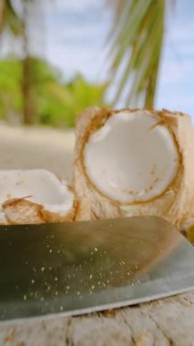 Dikey video. Bıçak ve Açılmış Hindistan cevizi Sandy Beach ve Palm Trees in Arkaplanda Tropikal Gıda Hazırlama Sahnesi ile Ahşap Kütüğe yerleştirildi