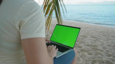 Palm Leaves Geniş Açı, Uzaktan Çalışmalar ve Dijital Göçebe Konsepti ile çevrili Yeşil Ekran Bilgisayarlı Kum Kumsalında Oturan Kişi