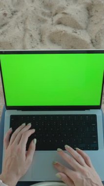 Dikey video. Kum Kumsalı 'nda, Uzaktan Çalışma Konsepti' nin yanındaki Yeşil Ekran ile Dizüstü Bilgisayarda Yazan Eller Görünümü