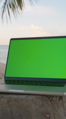 Dikey video. Kum ve Palmiye Yaprakları ile çevrili Tahta Kalaslı Laptop Okyanus Geniş Açısı, Uzaktan Çalışma ve Ada Yaşam Tarzı Konseptine Karşı