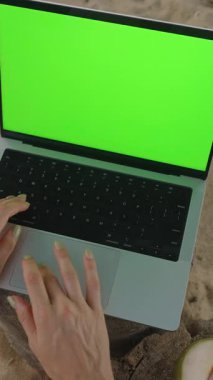 Dikey video. Eller Laptop 'ta Yeşil Ekran' la Kum Cevizi Yakınındaki Ahşap Kum Damlasında Yazıyor Yakın çekim, Uzaktan Çalışma Konsepti