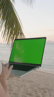 Dikey video. Palmiye Ağacının Altında Braid Duran Kadın Yeşil Ekran Geniş Deniz Açısı, Uzak Ofis Konsepti ile Laptop Kullanıyor