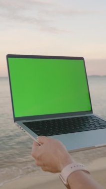 Dikey video. Okyanusa Bakan Yeşil Ekran ve Günbatımına Bakan Dizüstü Bilgisayarı Uzaktan İş ve Serbest Konsepti
