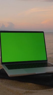 Dikey video. Sunset 'te Sandy Plajı' nda Yeşil Ekran 'da dizüstü bilgisayarla Hindistan cevizine uzanan Uzaktan Kumandalı Uzaktan Çalışma Konsepti