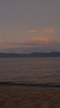 Dikey video. Geniş Tropikal Plaj Panoraması Gün batımında Geniş Dalgalar ve Uzak Dağlarla Gökyüzünde Renkli Bulutlar, Huzur Deniz Burnu Konsepti