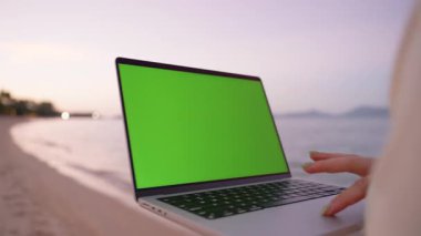 Plajda Dizüstü bilgisayarla yürüyen kadın, Sunset 'te okyanusta gezinirken daktilo, Mockup' ın Yeşil Ekranı