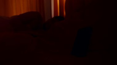 Smartphone Alarmına Ulaşan Adam Sabah 6 'da Loş Işıklı Yatak Odasında Düşük Açı Uyanış Sürecinden Turuncu Perdelerle