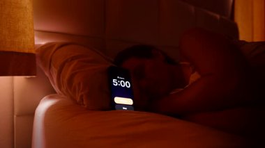 Sabahın 5 'inde yatakta uzanan, Smartphone Alarmı' nı kapatan, Parlak Pencereden dışarı bakan ve Sabah Tembelliği 'ni tekrar uykuya daldıran kadın.