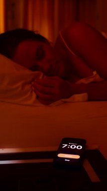 Dikey video. Sabah 7 'de Smartphone' da kadın alarmını kapatıyor. Sonra parlak bir sabahta pencereden dışarı bakıyor. Sabah Tembelliği 'ne tekrar dalmadan önce.