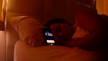Beyaz çarşafın altında yatan kadın sabah 7 'de alarmı kapatıyor. Parlak pencereden dışarı bakıyor ve yine geç saatte uyuyakalıyor.