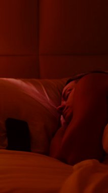 Dikey video. Smartphone 'da 6: 00 Alarmı Kapatılan Gözler Sabah Gevşemeden Önce Parlak Işıkla Pencereye Bakan Kadın