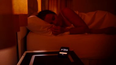 Sabah 7 'de Smartphone' da kadın alarmını kapatıyor. Sonra parlak bir sabahta pencereden dışarı bakıyor. Sabah Tembelliği 'ne tekrar dalmadan önce.