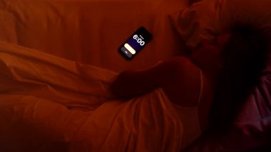 Smartphone Alarm 'ın yanında uzanan kadın sabahın 6' sında Perdelerden Parlak Turuncu Işık ile çalıyor.