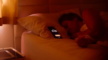 Sabah 6 'da beyaz çarşafların altında uzanmış, parlak pencereden dışarı bakan ve tekrar uykuya dalan kadın alarmını kapatıyor.