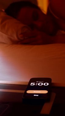 Dikey video. Akıllı telefondan sabah 5 'ten sabah 5' e kadar uzanan kadın. Sonra parlak bir sabahta pencereden dışarı bakan ve uykulu bir sabah rutini.