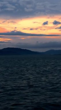 Vertical video. Moving Ship on Calm Sea During Sunrise with Cloudy Sky and Silhouetted Islands on Horizon Tranquil Morning Journey