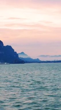 Vertical video. Ship Sailing Toward Mountain Islands During Sunrise with Soft Pink Sky and Calm Sea Morning Exploration