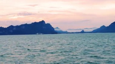 Moving Ship Crossing Calm Sea During Sunrise with Pink Orange Sky and Green Islands on Horizon Morning Calmness