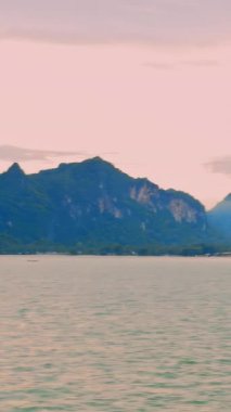 Vertical video. Peaceful Sunrise Over Sea Viewed from Moving Ship Passing Green Coastal Mountains Under Pink Blue Sky Tropical Journey