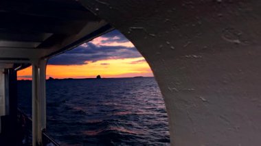 Ferry View Through Metal Frame Toward Bright Orange Sunset Over Calm Sea with Distant Islands Evening Serenity